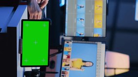 Vertical video Green screen tablet on desk in photography studio next to photo editor looking at pictures taken with professional camera for fashion magazine. Mockup device near photographer working