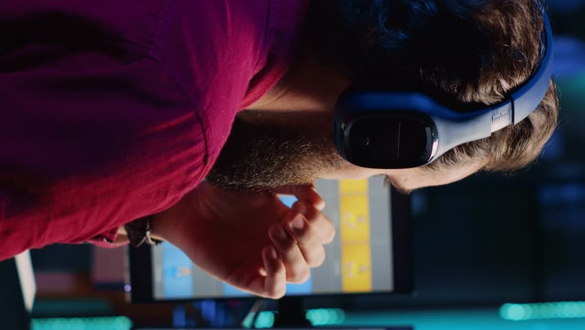 Vertical video Photo editor tired after retouching images with editing software all day, taking break by looking at funny videos on smartphone. Photographer relaxing after adjusting images, looking at