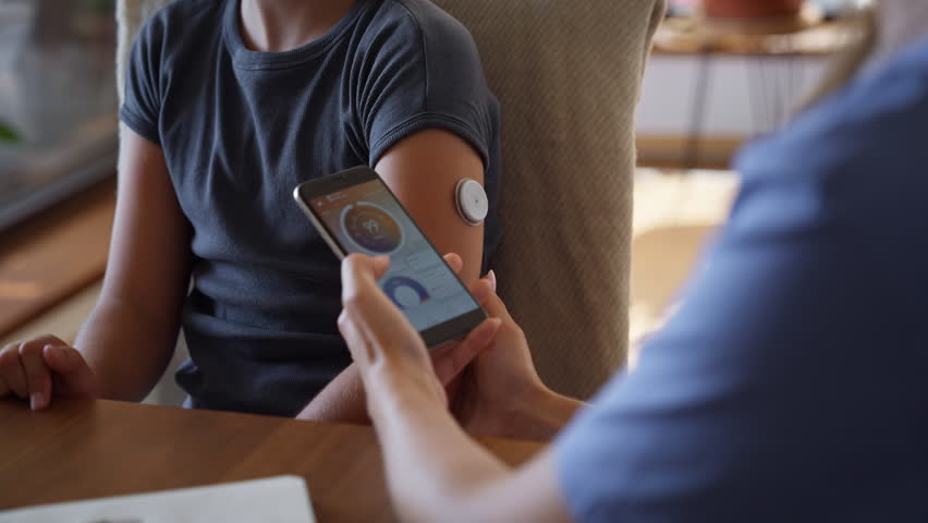 Girl with diabetes checking blood glucose level at home using continuous glucose monitor.