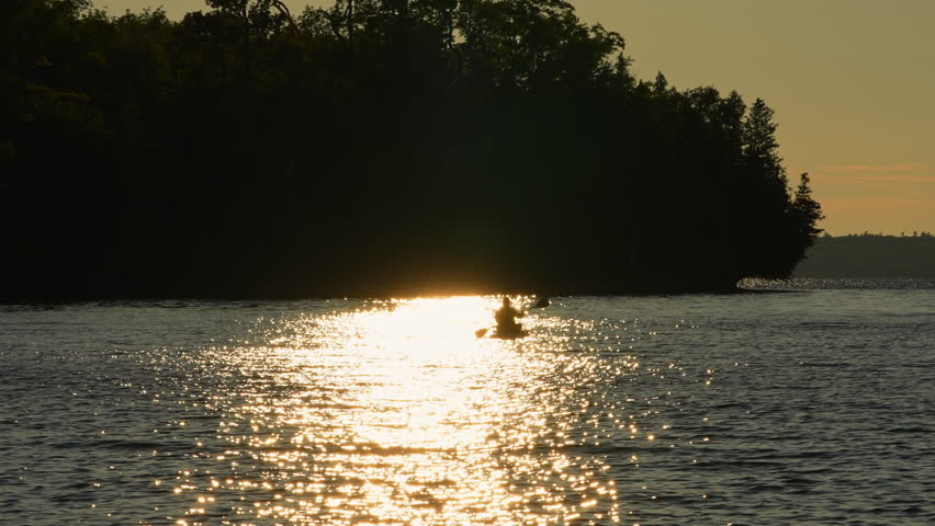 Woman glides on a paddleboard during the tranquil golden hour sunset on a serene lake, enjoying the warmth of summer. Engaging in the stand-up paddleboard SUP sport, relaxation at Lake Manitou.