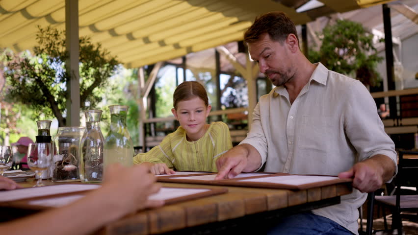 Father and daughter reading menus in a restaurant, choosing food and drinks.