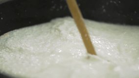 Fermented milk mixed in bucket with a wooden ladle. Cheese and Curd production Technology. Slow motion clip
