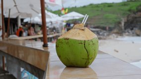 Video footage of green young fresh coconut with straw. Close up on the beach in Bali. Slow motion