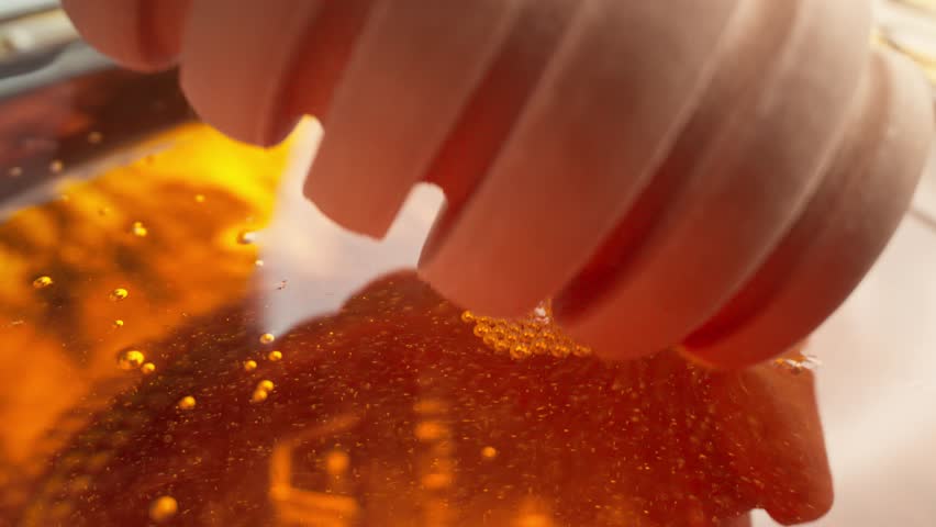 Honey dripping. Pouring honey in bowl. Dipping honey with honey scoop in glass jar. Healthy organic food. Close-up in 4K, UHD