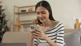 young Asian woman confidently using a smartphone, texting, chat with friends and video call sitting on a beige couch with a white cushion. - Powered by Shutterstock - Get 15% off with code: PIKWIZARD15