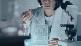 Female scientist dropping liquid chemical into test tubes on a rack, carrying out medical research in the laboratory. Selective focus shot - Powered by Shutterstock - Get 15% off with code: PIKWIZARD15