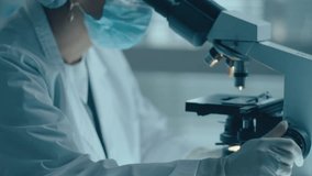 Female laboratory technician in protective mask, hat and gloves looking through microscope and writing down results of medical test - Powered by Shutterstock - Get 15% off with code: PIKWIZARD15