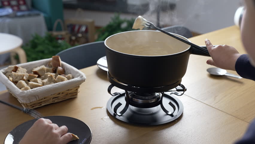 Traditional Swiss Fondue - people eating pieces of bread with cheese at home, close-up of European dish from Switzerland