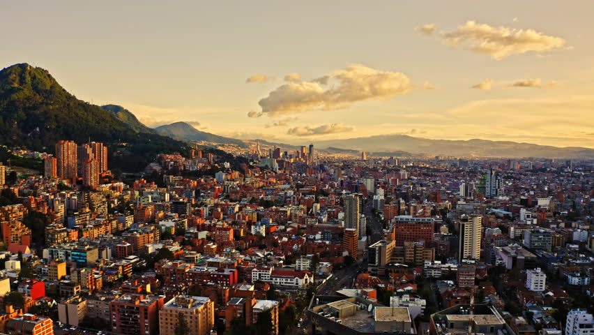 Cinematic high view over Bogotà, capital of Colombia. View of the majestic mountains in the background. Warm sunset sky. Drone shot over Bogotà at golden hour.
