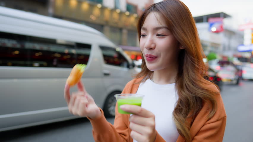 Young Asian tourists standing and eating Thai desserts. Young beautiful tourists in Chinatown street food market, Bangkok, Thailand