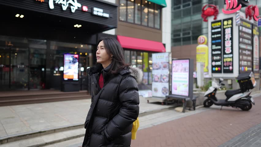 A South Korean man in his 30s with long hair, sightseeing in the winter snowfall on a street in Myeongdong, Seoul, South Korea.