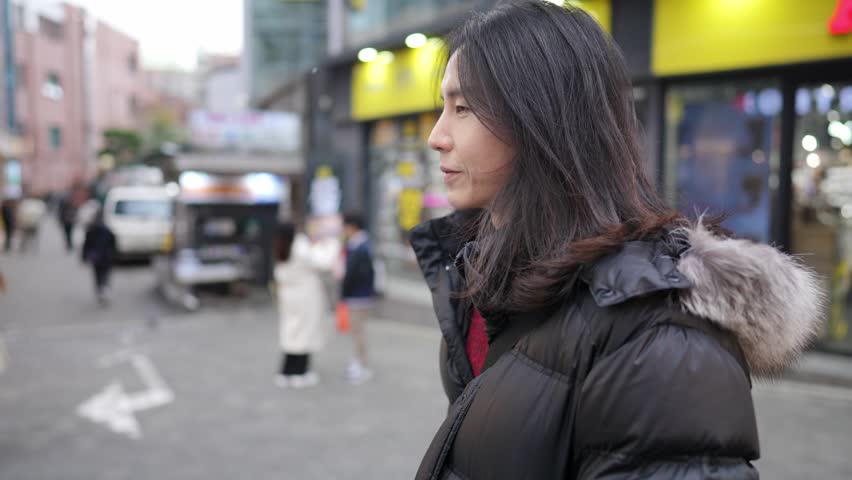 A South Korean man in his 30s with long hair, sightseeing in the winter snowfall on a street in Myeongdong, Seoul, South Korea.
