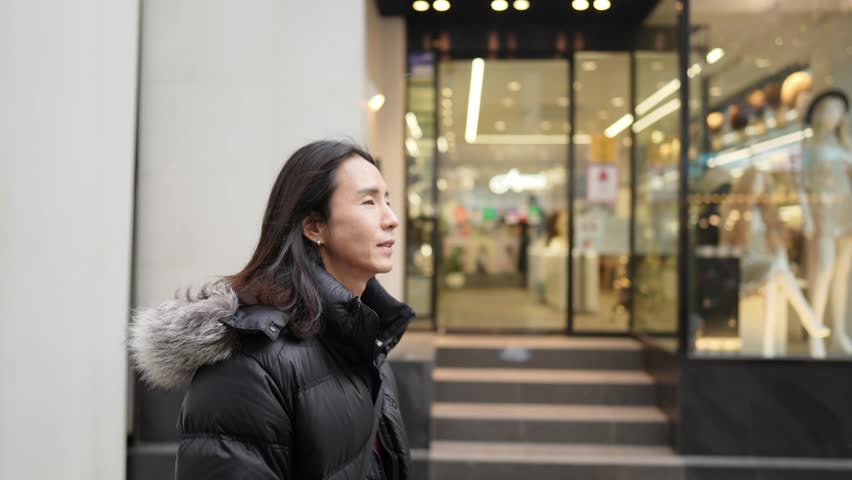 A South Korean man in his 30s with long hair, sightseeing in the winter snowfall on a street in Myeongdong, Seoul, South Korea.