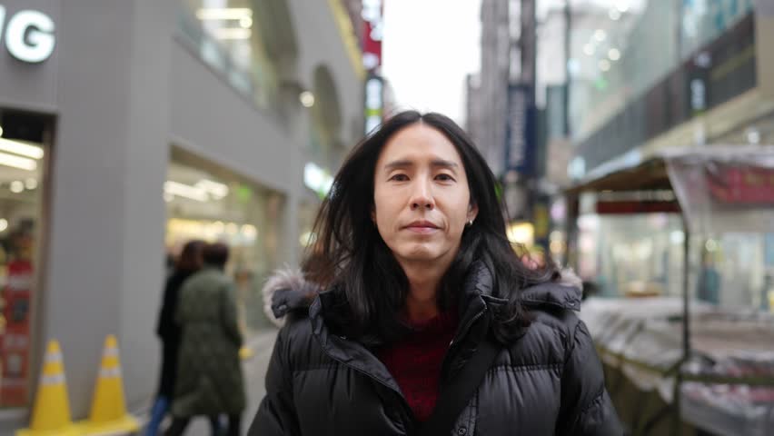 A South Korean man in his 30s with long hair, sightseeing in the winter snowfall on a street in Myeongdong, Seoul, South Korea.
