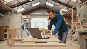 Male carpenter working in woodwork workshop talking on mobile phone whilst using laptop - shot in slow motion - Powered by Shutterstock - Get 15% off with code: PIKWIZARD15