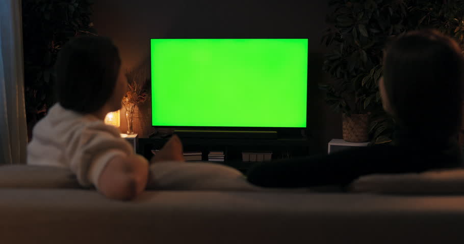 Green screen mockup tv. Over the shoulder shot two women friends sitting in the living room watching tv films movie news talking spending time together resting after hard day at work weekend time.