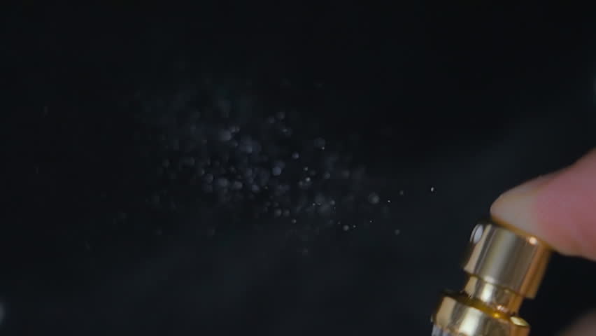 The finger presses the bottle cap with perfume and the liquid flies in small drops and hangs in the air on black background. Closeup. Slow mo, slo mo, slow motion, high speed camera, 240fps, 250fps