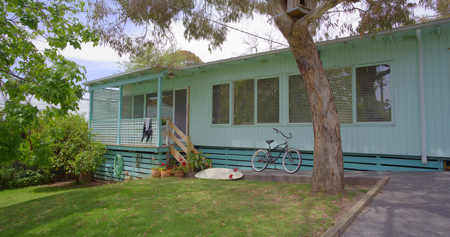 A surfer leaves his beach house gathers his wetsuit and bicycle and heads of to the beach.