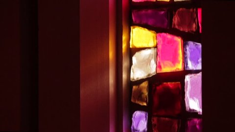 Camera pans on contemporary, abstract stained glass window in a chapel or church as sunlight streams through it