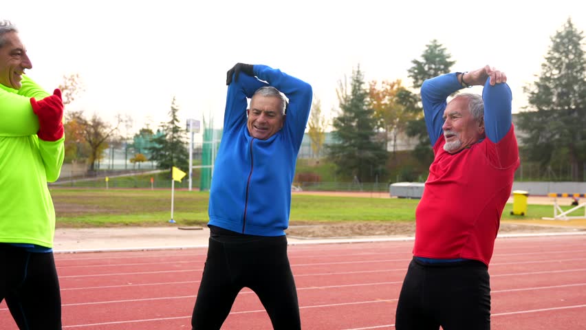 Smiling elder man with sports clothes warming up in a track and field in winter