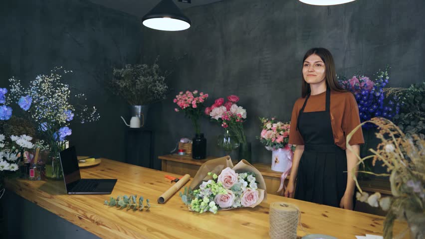 A young woman florist in a flower shop gives a bouquet to the customer. Buyer of a bouquet. Retail sale of flowers.