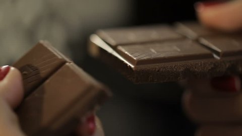 Woman breaks chocolate bar. Hands breaking, cracking dark milk chocolate. Person chef chocolatier snapping apart pieces of sweet chocolate for melting and making sweets desserts. Slow motion