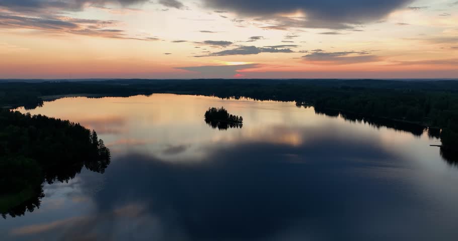 Aerial view of sunset in the misty finnish forest. Flying over a lake with reflections in Finland. Drone landscape video of evening sunset. A nordic sunset over lake. Scenic colorful nature landscape.