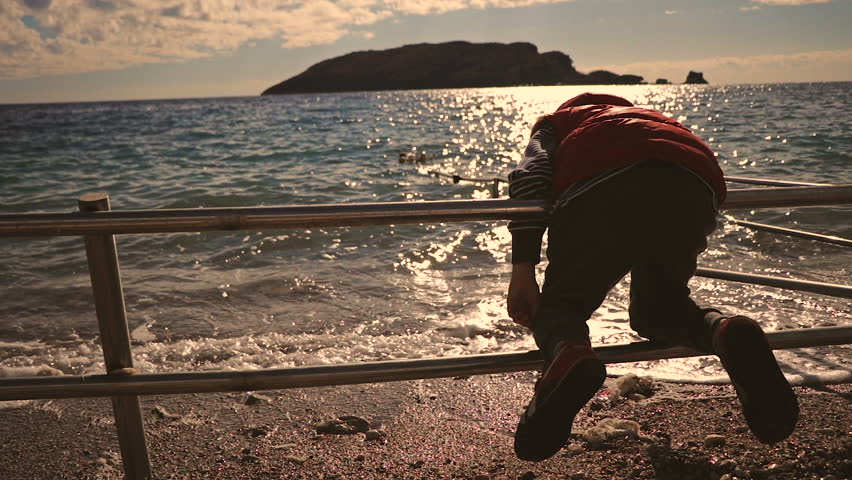 The child is 8 years old. Playing on the beach with a stick on sunset