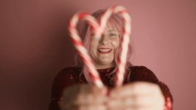 Portrait of young beautiful Caucasian woman in dress hands gesture in heart shape with candy canes poses against pink background. Valentine's day. High quality FullHD footage - Powered by Shutterstock - Get 15% off with code: PIKWIZARD15