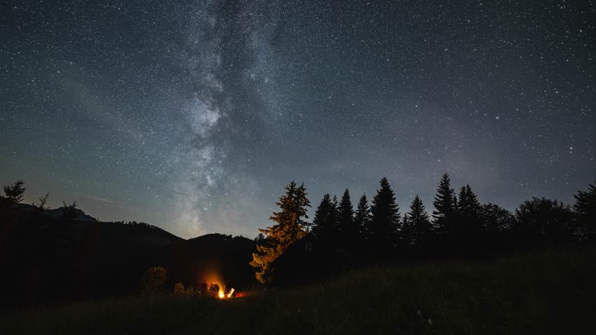 Friends sitting by campfire under starry night sky with milky way galaxy stars over forest nature Astronomy Time lapse Outdoor adventure