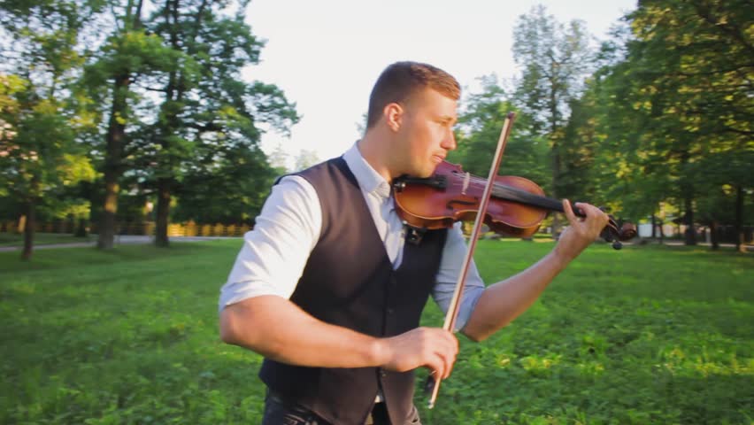 Man playing the violin . young musician artist violinist enthusiastically with violin in hands in vest and shirt ,playing the violin in the park .concept hobby music public performance practice Royalty-Free Stock Footage #3394500945