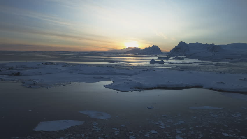 Dawn over Antarctic coast. Polar night sunset. Ocean covered ice. Top above aerial view. Antarctica snow mountain. Sky sunrise Antarctica winter. Open water. Beautiful sky landscape. Top Drone Flight
