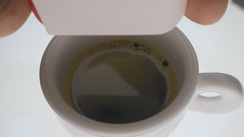 The hand presses the button and the sugar substitute tablet drops out of the box and falls down into a cup of coffee. Closeup. Slow mo, slo mo, slow motion, high speed camera, 240fps, 250fps