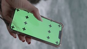 Vertical video. View from Behind the Head of a Woman with Long Hair, Swiping Sideways with a Large Finger on the Green Screen with Markers for a Mockup. Against the Background of Windy Weather and Sea
