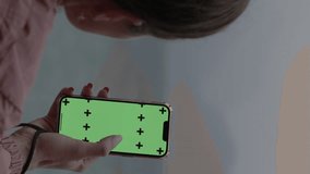 Vertical video. View from Behind the Head as a Woman Scrolls Through the Feed with a Large Finger on the Green Screen for a Mockup, Inserting Her Video at the Markers. In the Background, There Is the 