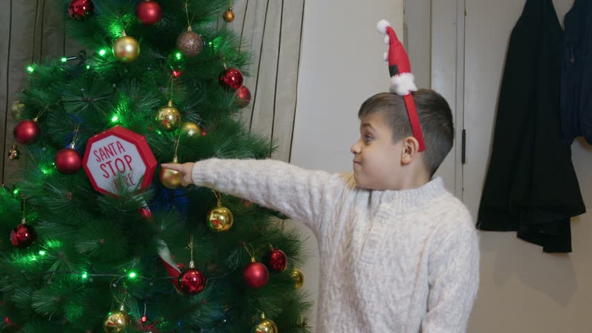 Adorable children playing in front of Christmas tree. Boy pointing finger on the sign Santa stop here and winking. High quality 4k footage