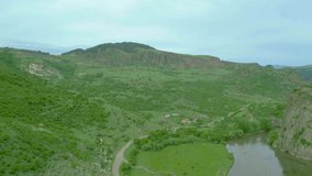 An aerial view of high rocky mountains covered with green grass and trees on an overcast summer day. Small villages near the river with country roads. Dzoraget River, Canyon, Armenia. Drone footage