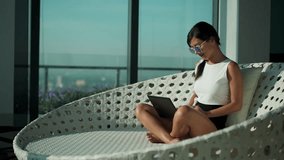 Young Asian business woman wear suit sit on couch chair working on laptop in modern modern business lounge office. Gorgeous lady freelancer digital nomad concept. Working online. Urban background