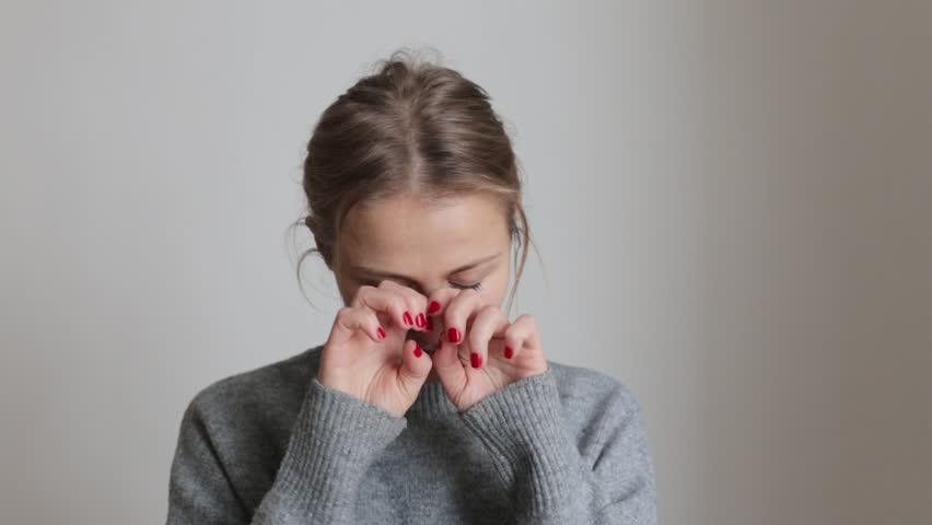 A young girl in a cozy gray sweater rubs her eyes from fatigue. The girl rubs her eyes. Dryness and allergic reaction, the girl rubs her eyes with her hands Royalty-Free Stock Footage #3394997081