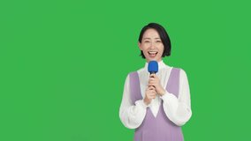 An Asian reporter reporting with a microphone. Green background for chroma key composition.