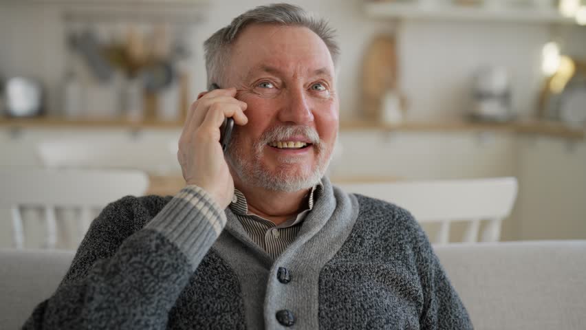 Positive senior man calls phone at home. Portrait old gray haired male talking on smartphone sitting on couch, smiling laughing enjoying conversation with friend, relative. Happy sociable person. Royalty-Free Stock Footage #3395088129