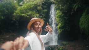 Follow me woman near tropical waterfall. Blonde smiling female tourist in straw hat holding man's hand following him to waterfall. Travel tourism vacation, summer holidays concept. Travelling couple. - Powered by Shutterstock - Get 15% off with code: PIKWIZARD15