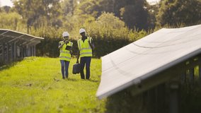 Male and female engineers wearing hard hats and hi vis safety vests with digital tablet walking through field outdoors inspecting solar panels on sustainable energy farm - shot in slow motion - Powered by Shutterstock - Get 15% off with code: PIKWIZARD15