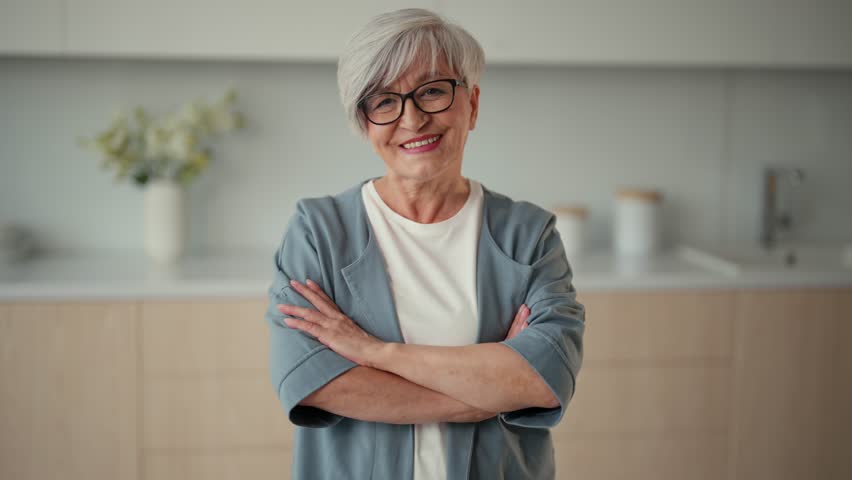 Portrait happy senior woman standing on kitchen at home in closed pose with hands on chest looking at camera, Gray haired retired good looking pensioner female in glasses. Old age lifestyle concept. - Powered by Shutterstock - Get 15% off with code: PIKWIZARD15