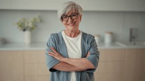 Portrait happy senior woman standing on kitchen at home in closed pose with hands on chest looking at camera, Gray haired retired good looking pensioner female in glasses. Old age lifestyle concept. - Powered by Shutterstock - Get 15% off with code: PIKWIZARD15