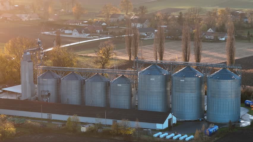 Agricultural storage silos shine in the evening sun, towering over a village surrounded by fall fields.