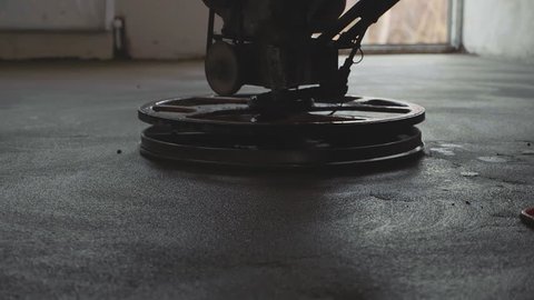 Builder polishing mortar floor at construction site of new appartments. Mechanized grout screed concrete floor close-up slow motion