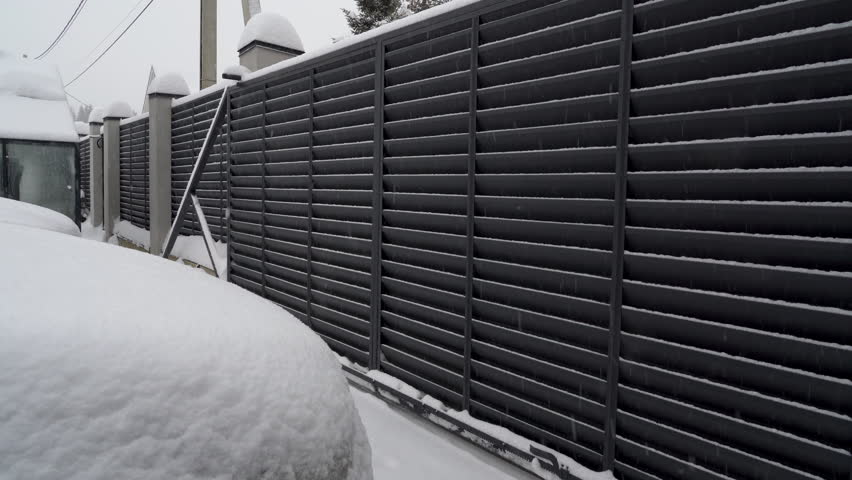 View of automatic gate closing at snowy winter day. Modern design motorized automatic driveway gate, fence gate of courtyard of residential building in winter. Royalty-Free Stock Footage #3395161043