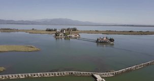 Aerial wide shot of lagoon with church, with drone flying backwards, birds enter the shot