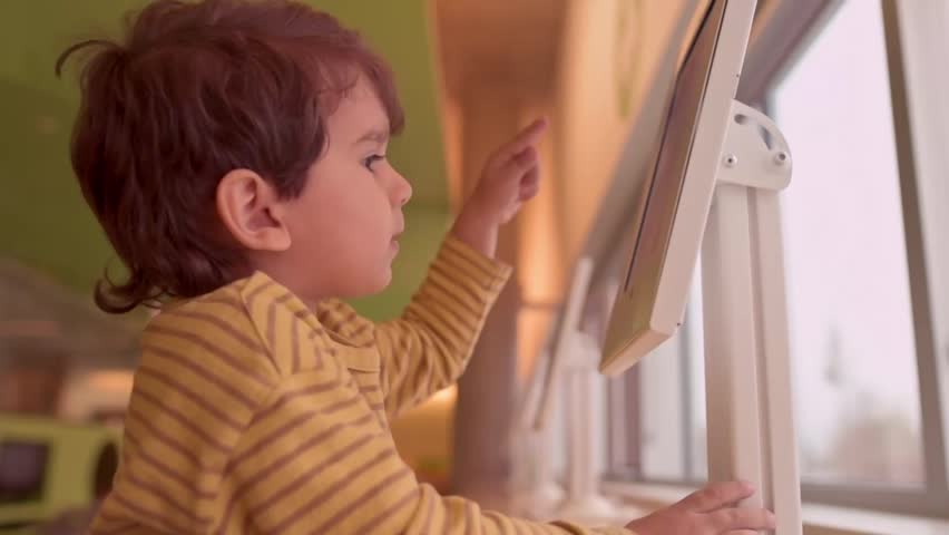 Happy little Caucasian kid smiling and watching something on digital tablet indoor at library